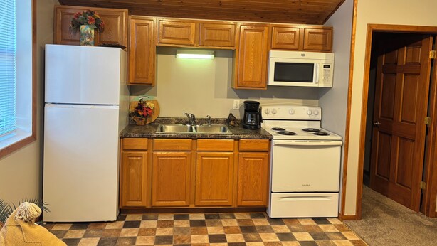 Une cuisine avec des meubles de rangement en bois, un réfrigérateur, un four à micro-ondes, une cuisinière et un évier.