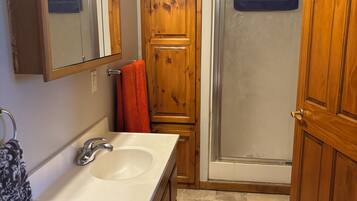 Een badkamer met een houten wastafelmeubel, een wastafel, een spiegel en een douche.
