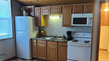 A compact kitchen with wooden cabinets, a refrigerator, a microwave, a stove, and a sink.