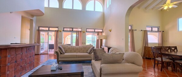 A spacious living room with a large sofa, a coffee table, and a dining area with wooden chairs.