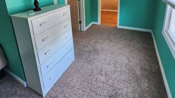 Una habitación con paredes verde azulado, un tocador blanco, una lámpara y una puerta que da a otra habitación.