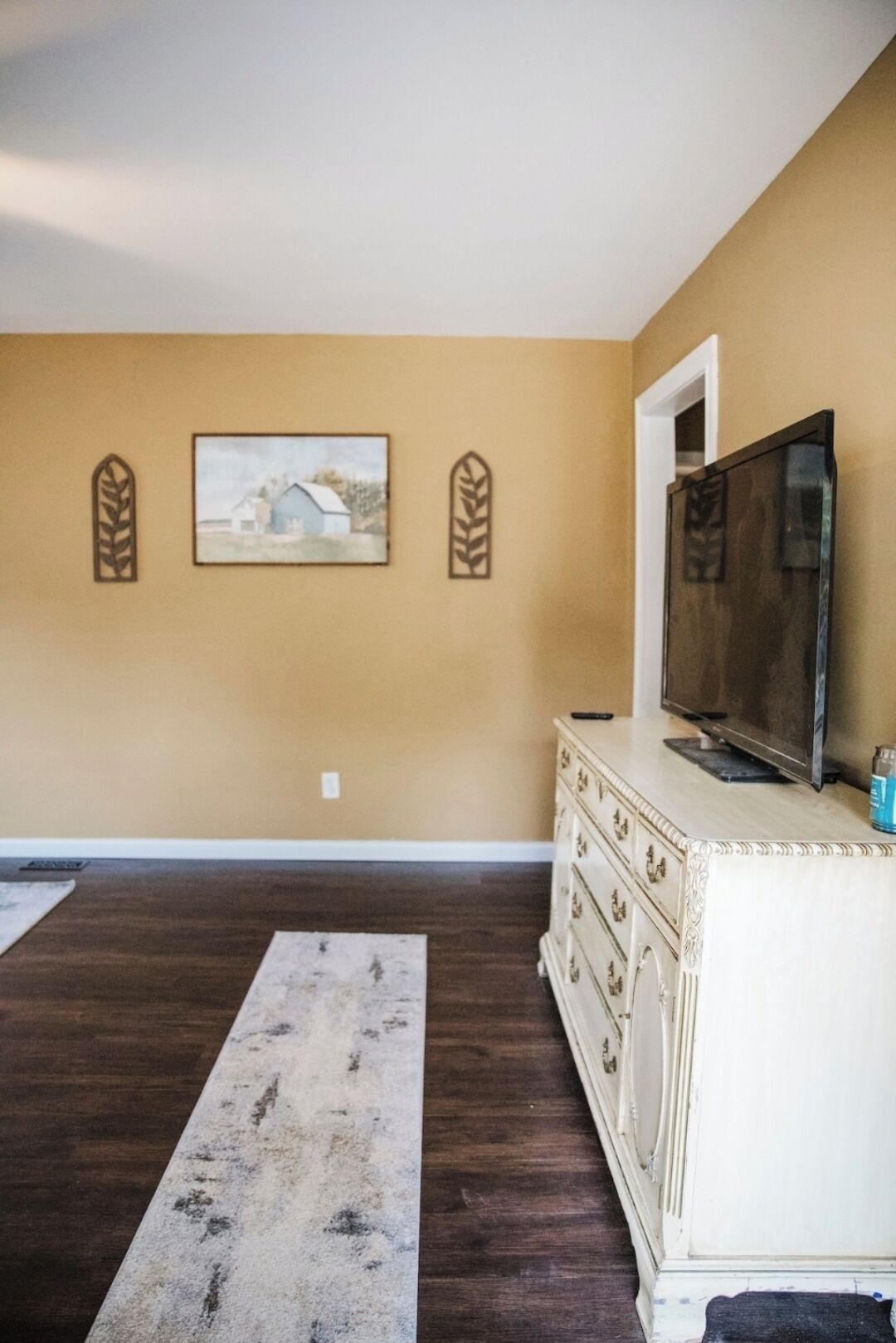 Um quarto com parede marrom, cômoda branca com televisão e tapete.