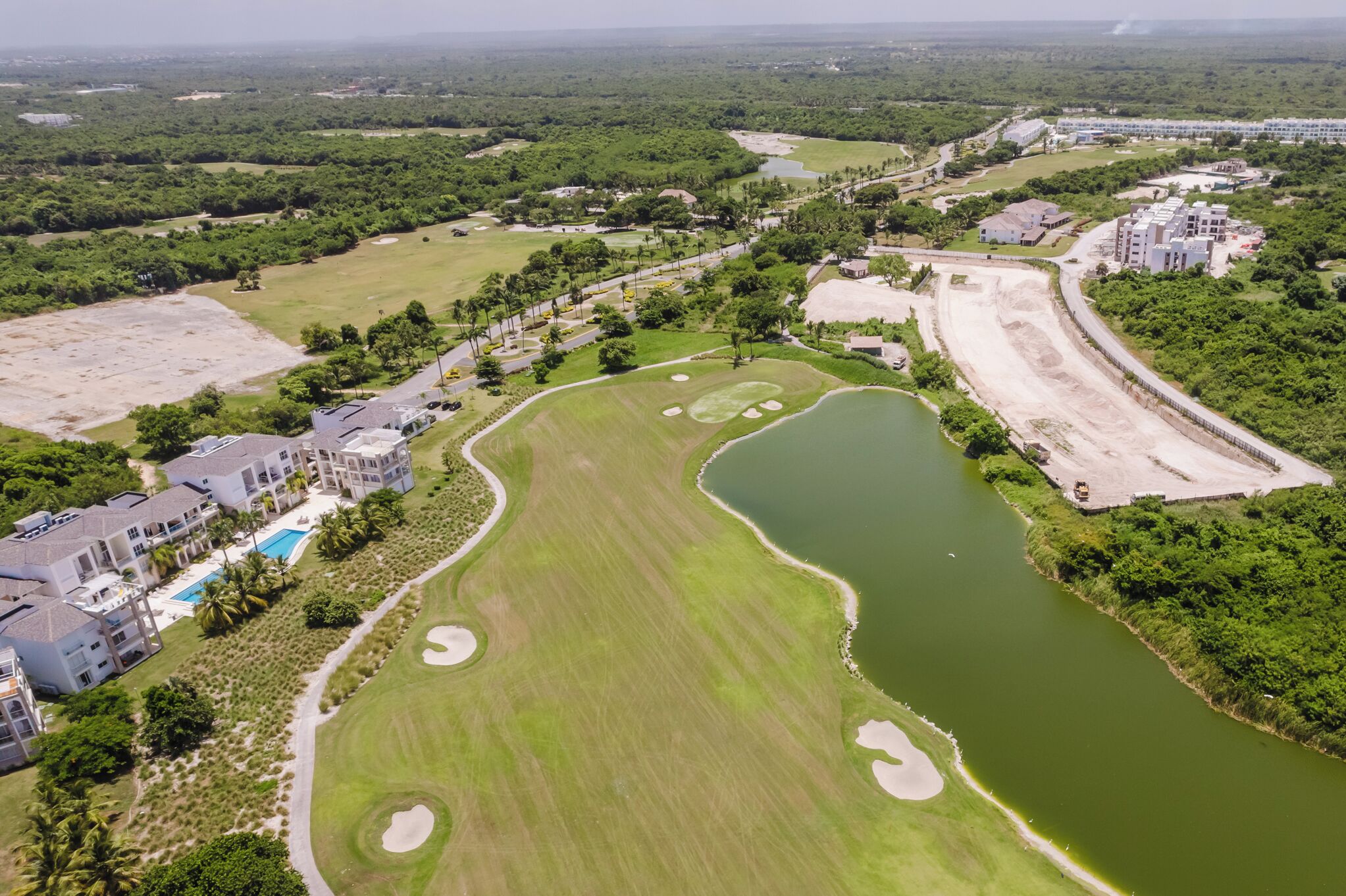 An aerial view of a golf course with a large pond, surrounding buildings, and a parking area.