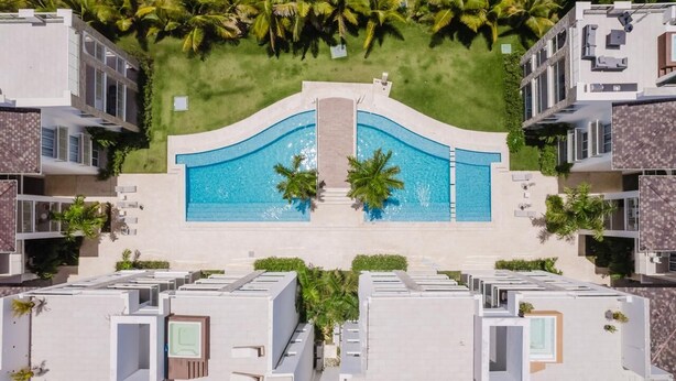 Ein modernes Hotel mit einem zentral gelegenen Schwimmbad, umgeben von üppiger Vegetation und Palmen.