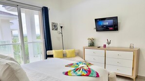 Ein Schlafzimmer mit Bett, Fernseher, Kommode und Blick ins Freie.