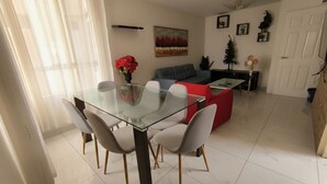A dining area with a glass table and chairs, a red sofa, and a small plant on a side table. - Cozy central shelter, steps away from the Mall (Ideal for families and friends). (Trujillo)