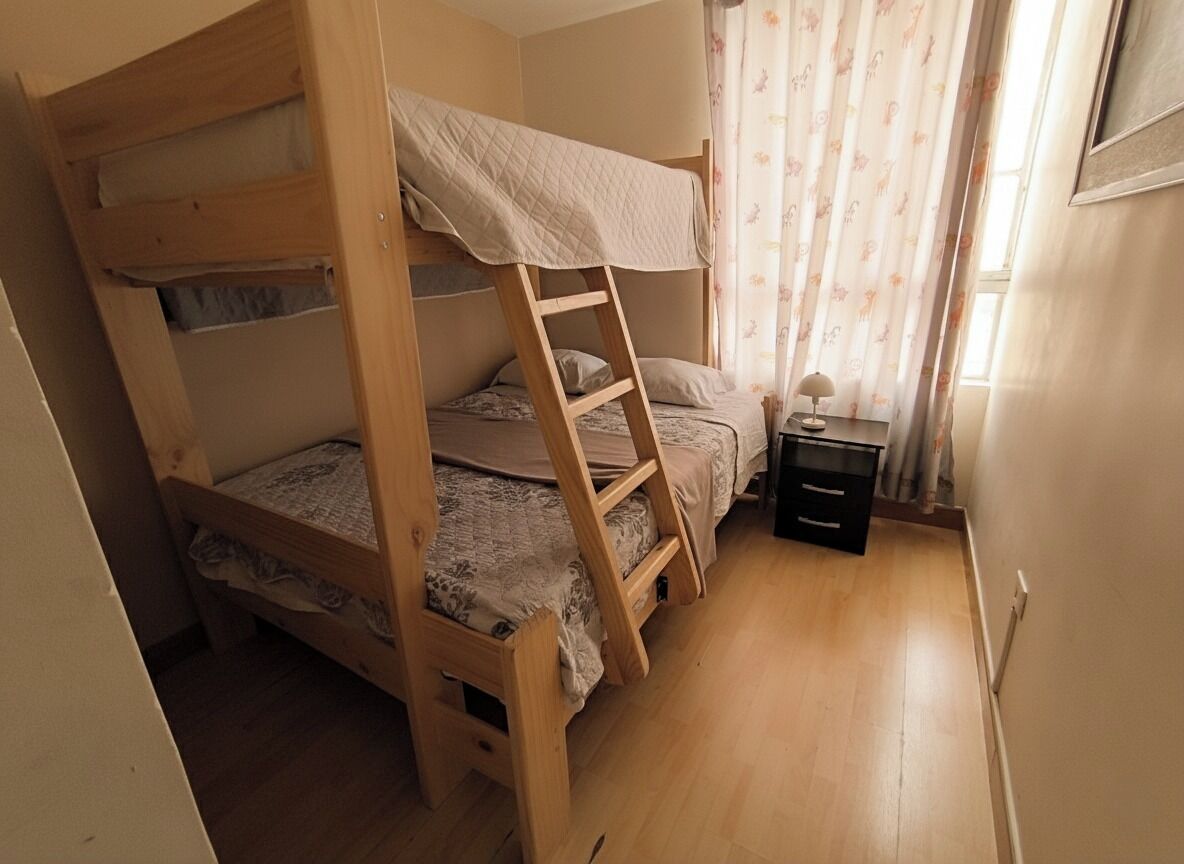 Habitació amb lliteres, una tauleta de nit amb una làmpada i una finestra amb cortines.