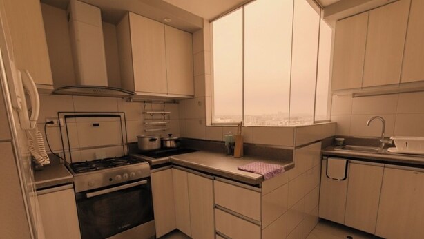 A compact kitchen with a gas stove, oven, and a window overlooking a cityscape. - Cozy central shelter, steps away from the Mall (Ideal for families and friends). (Trujillo)