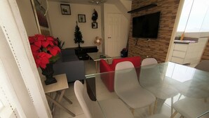 A modern dining area with a glass table and chairs, a red couch, and a small Christmas tree. - Cozy central shelter, steps away from the Mall (Ideal for families and friends). (Trujillo)