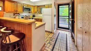 A kitchen with wooden cabinets, a microwave, a refrigerator, and a bar area with stools. - Bear Hills Retreat with Scenic Fairway Views (Hill City)