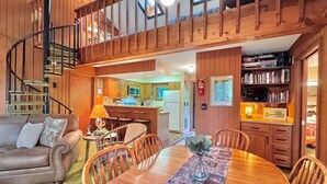 A cozy living room with a wooden dining table, a sofa, and a staircase leading to an upper level. - Bear Hills Retreat with Scenic Fairway Views (Hill City)