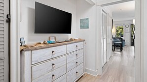 A hallway with a wooden dresser, a flat-screen TV, and a welcome sign. - Beachfront Couples Coastal Getaway
Oceanview I Pool I Balcony  AC
Parking I WIFI (Hilton Head Island)