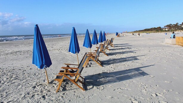 A beach with rows of blue umbrellas and wooden beach chairs. - Beachfront Couples Coastal Getaway
Oceanview I Pool I Balcony  AC
Parking I WIFI (Hilton Head Island)