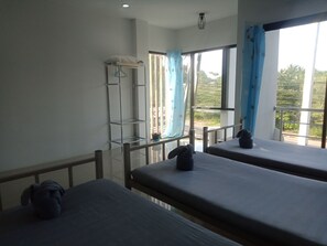 A hotel room with two beds, a window with blue curtains, a metal shelf, and a view of greenery outside. - Mangkonlay Hostel Krabi (Krabi)