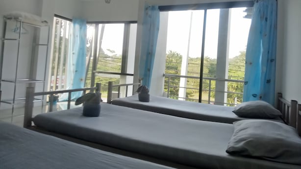 A room with two beds, a window with curtains, an air conditioning unit, and a view of greenery outside.