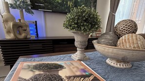 A welcome booklet titled 'BALAYCATION' on a table, a decorative bowl with spherical objects, a potted plant, and a television displaying a castle landscape. - Balaycation 3 BR, 2BA, 5 Beds, sleeps 8 (Davao City)