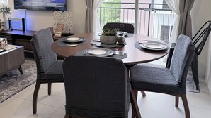 A dining area with a round table, four chairs, a TV mounted on the wall, and a balcony with a view of buildings. - Balaycation 3 BR, 2BA, 5 Beds, sleeps 8 (Davao City)