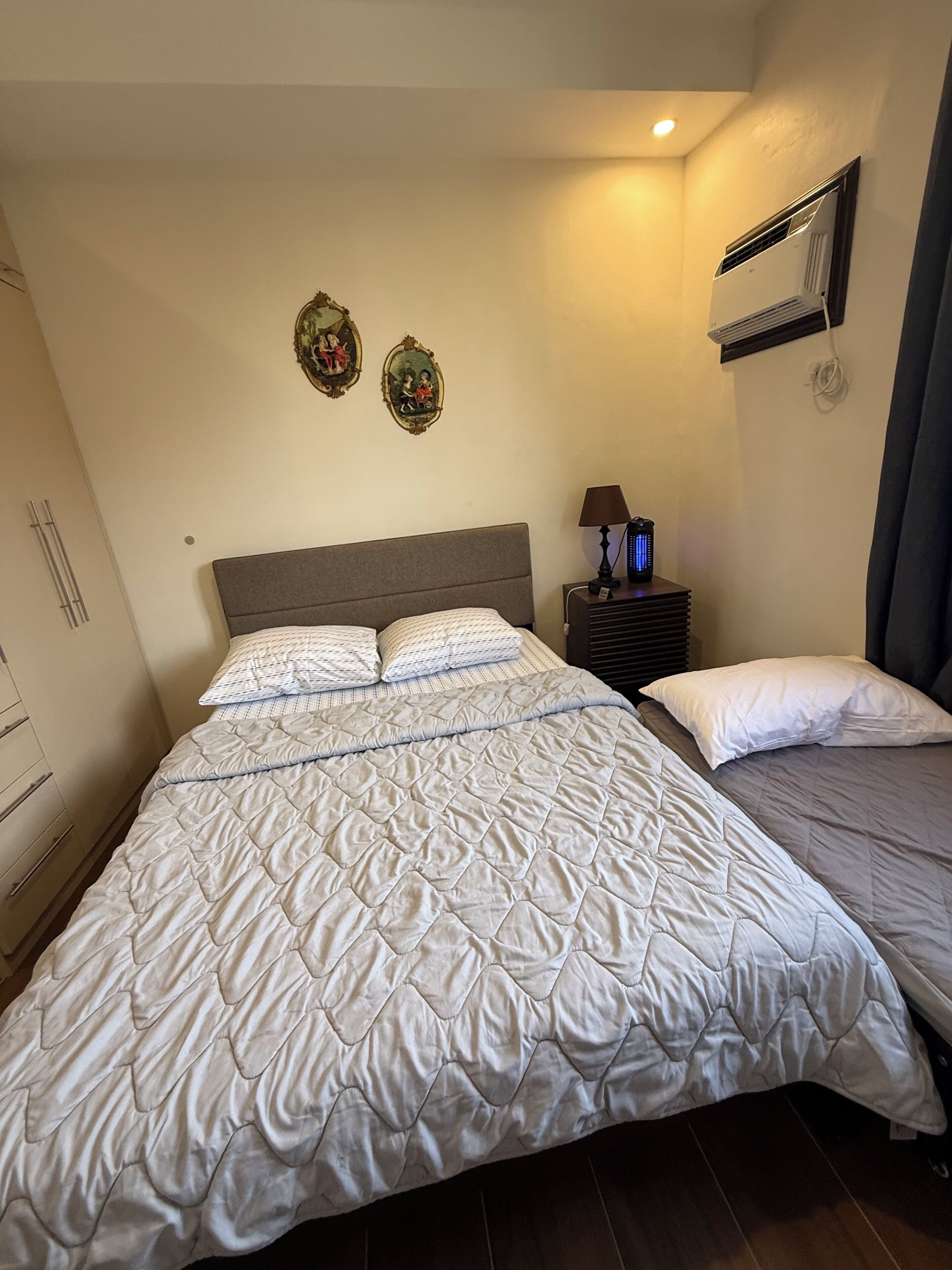 Ein Schlafzimmer mit einem großen Bett, Nachttischen, einer Wand-Klimaanlage und einer kleinen Lampe.
