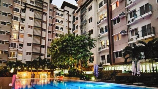 A swimming pool surrounded by multi-story residential buildings with balconies and air conditioning units. - Balaycation 3 BR, 2BA, 5 Beds, sleeps 8 (Davao City)