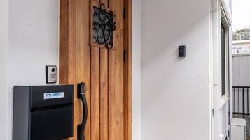 Een houten deur met een keypad-slot, een intercom bevestigd aan de muur, en een klein buitenruimte zichtbaar door een geopende deur.