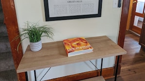 Une photographie encadrée des chutes de Great Falls est accrochée au mur, une plante en pot est posée sur une table en bois, et un livre intitulé « La vie en couleurs » se trouve également sur cette table.