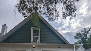 Une maison à deux étages avec un toit végétalisé, un revêtement extérieur blanc et une véranda à l’avant, dotée d’une terrasse en bois.