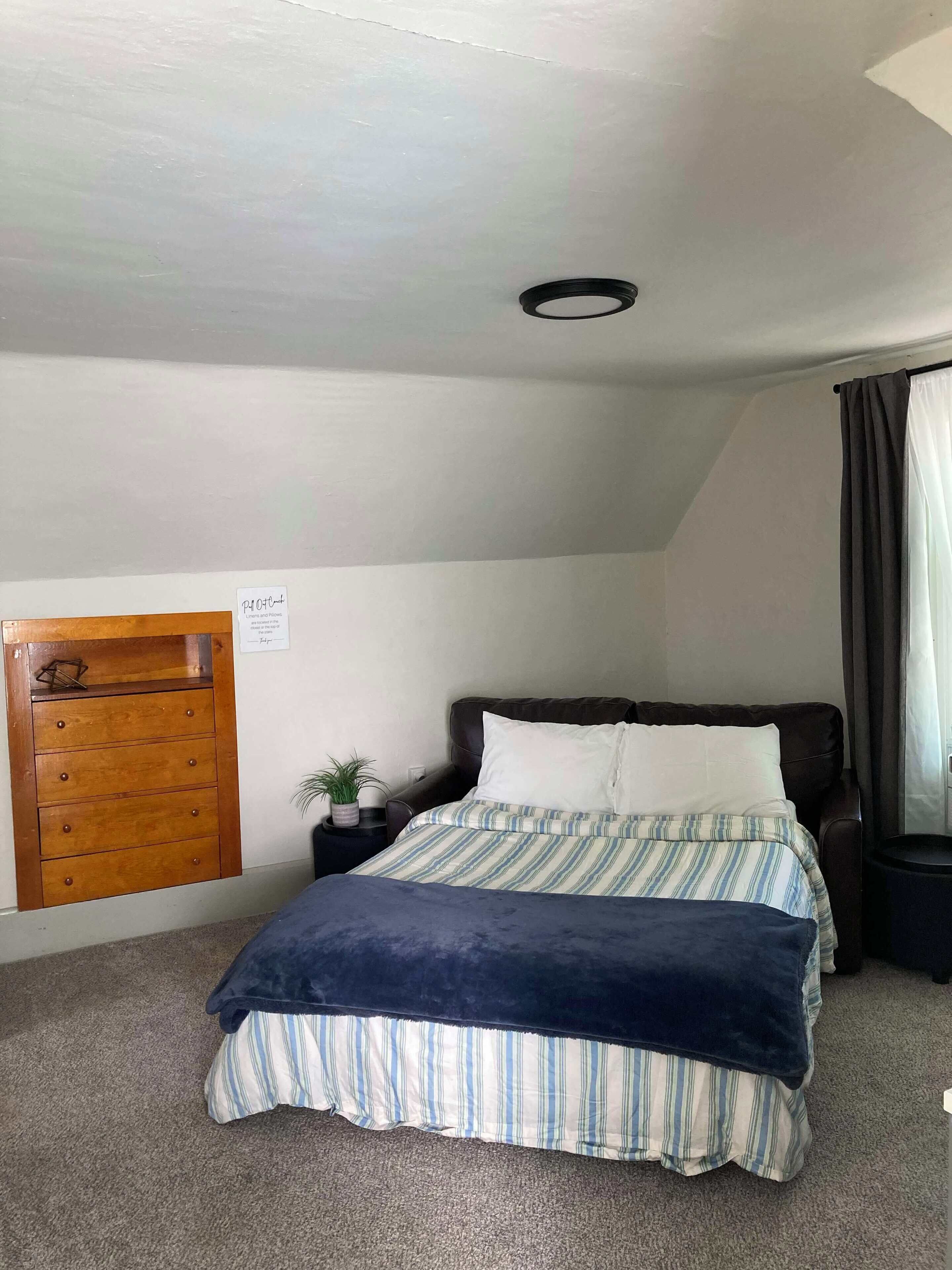 A bedroom with a bed, a dresser, a potted plant, and a window with curtains.