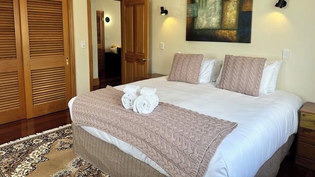 A neatly arranged bedroom with a large bed, wooden wardrobes, a ceiling fan, and a painting on the wall.