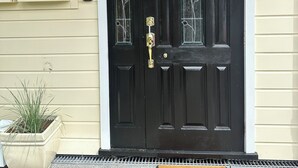 A black front door with a brass knocker, a doormat with "Hello!" written on it, and a potted plant beside the door.