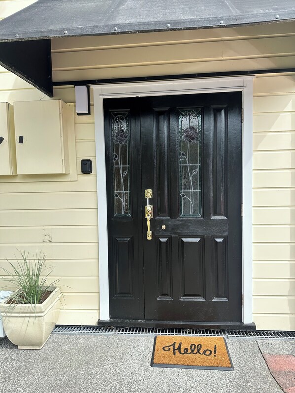 A black front door with a brass knocker, a doormat with "Hello!" written on it, and a potted plant beside the door.