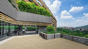 A modern building with a rooftop terrace featuring wooden flooring, outdoor seating, and lush greenery. - Chongqing Ronghui Grand Hotel (Chongqing)