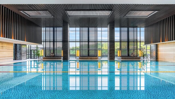 A modern indoor swimming pool with a clear view of the sky through large windows, a tiled floor, and a wooden ceiling. - Chongqing Ronghui Grand Hotel (Chongqing)
