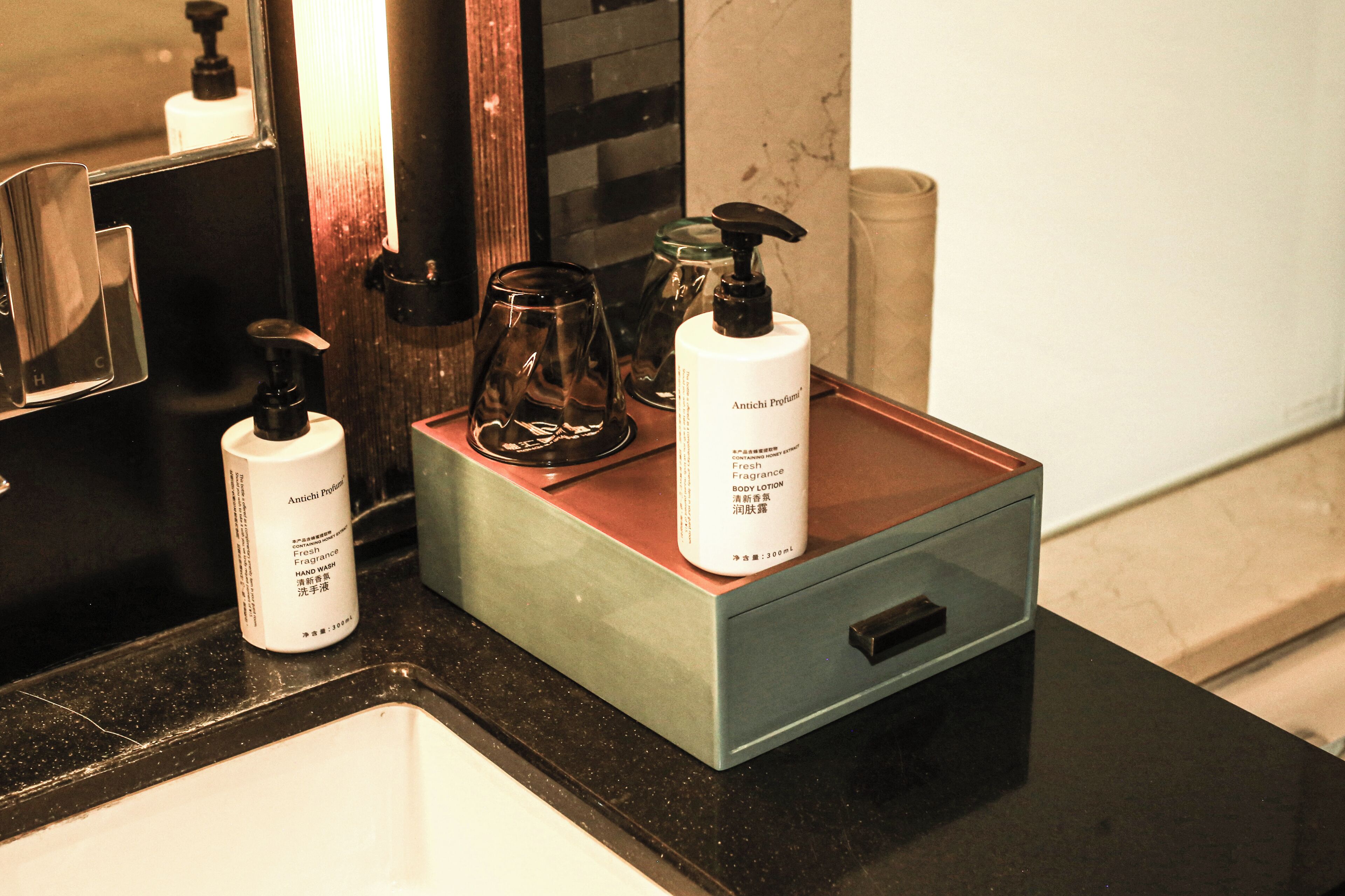 A bathroom counter with a soap dispenser, a glass container, and a bottle of body lotion.