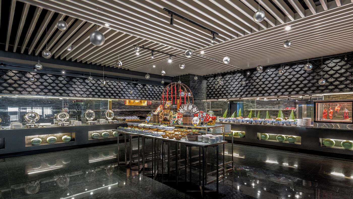 Interior de restaurant modern amb una illa central, seients escalonats i un sostre amb disseny.