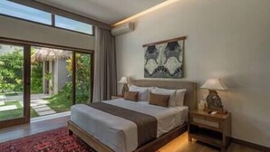 A bedroom with a large bed, a nightstand, a wall-mounted lamp, and a window with a view of greenery. - Villa Emmy | Elegant Seminyak 4BR Villa — Pool & Private Chef (Seminyak)