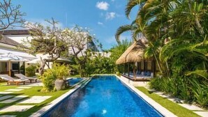 A swimming pool with lounge chairs and a thatched-roof structure, surrounded by lush greenery. - Villa Emmy | Elegant Seminyak 4BR Villa — Pool & Private Chef (Seminyak)