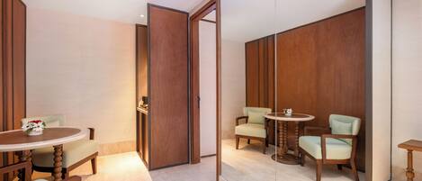 A room with a wooden wardrobe, a round table with chairs, and a mirror reflecting the room.