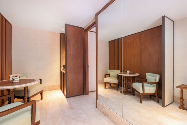 A room with a wooden wardrobe, a round table with chairs, and a mirror reflecting the room.