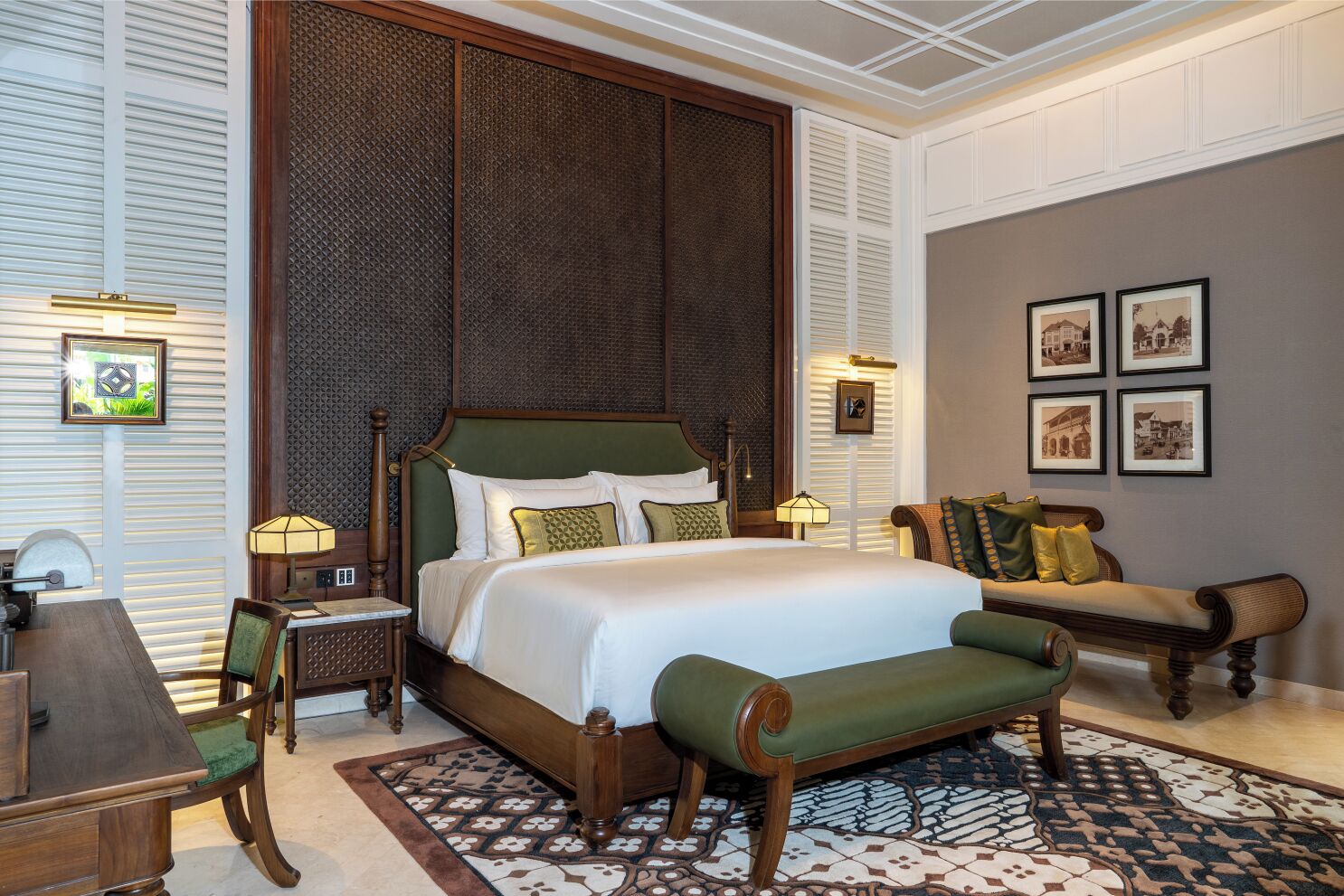 Une chambre élégamment aménagée, dotée d’un grand lit, d’un coin salon avec un banc et d’un mur orné de tableaux encadrés.