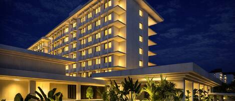 A multi-story hotel with a modern design, featuring balconies on each floor and a well-lit entrance area.