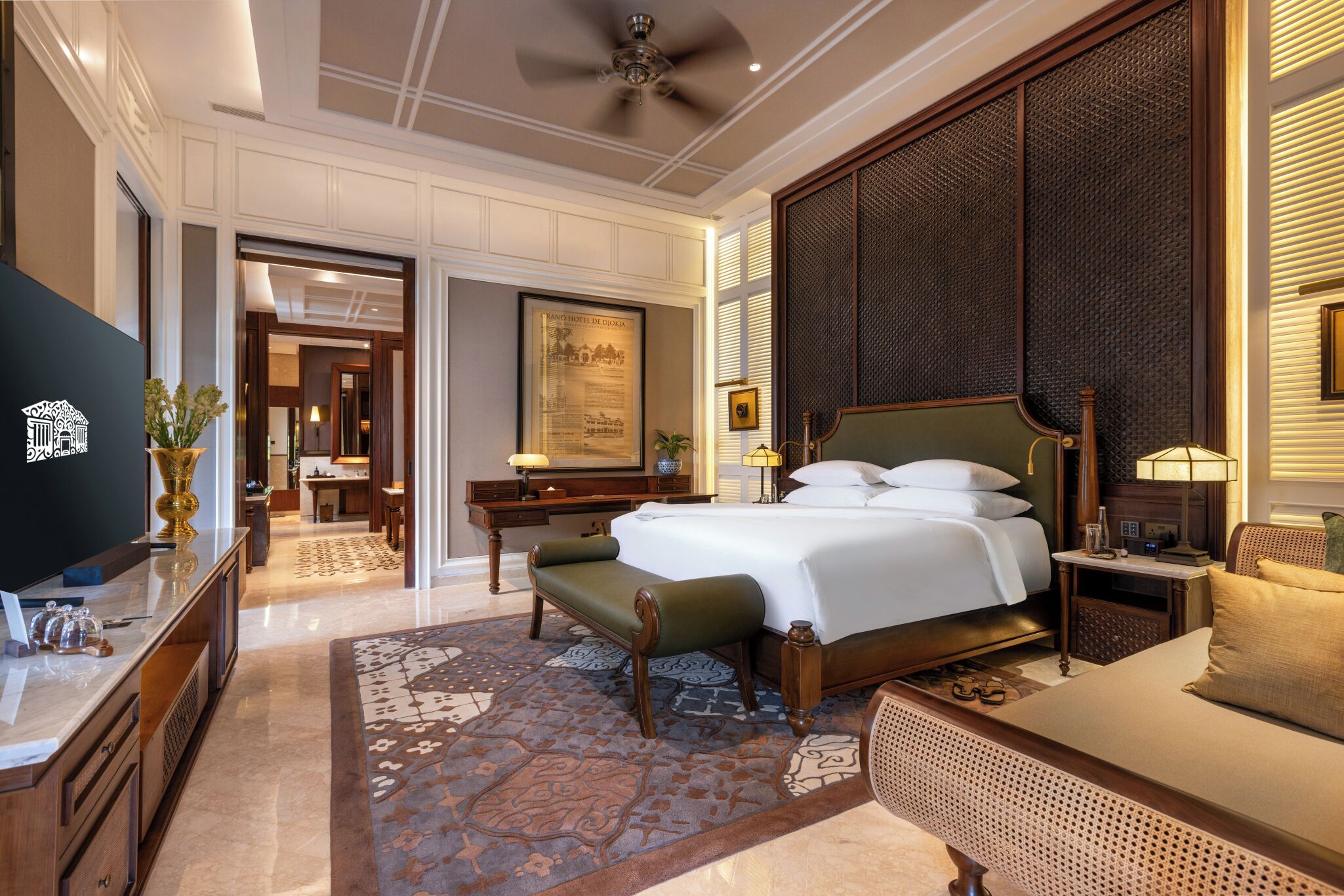 Habitación de hotel con cama, mesita de noche, lámpara y televisor sobre un soporte.