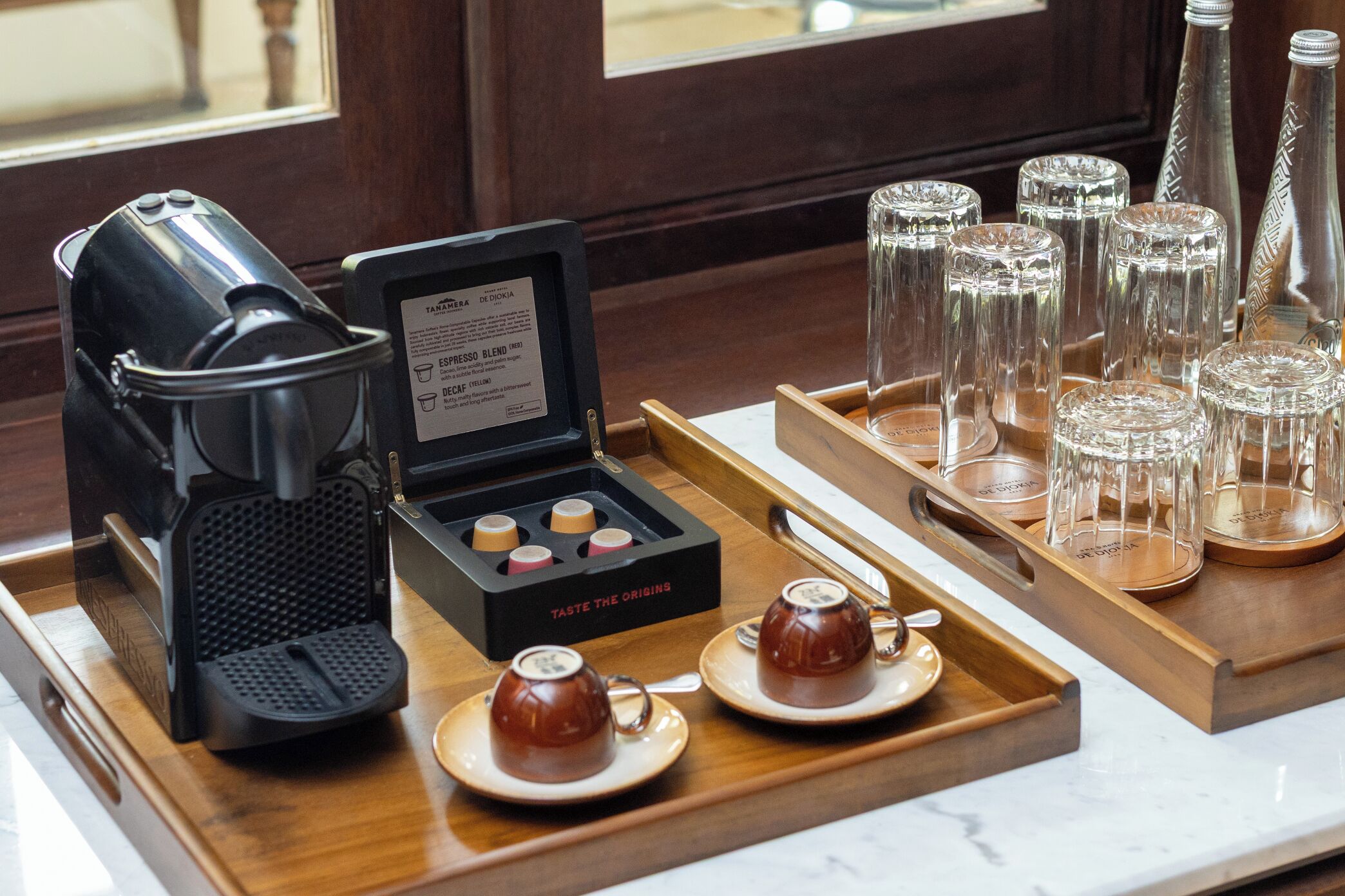 A coffee station with a coffee maker, a box of coffee pods, and a tray with cups and glasses.
