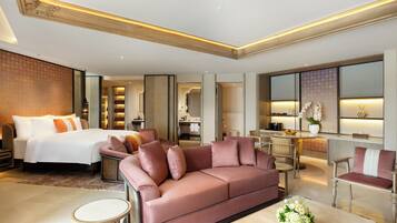 A modern hotel room with a large bed, a pink sofa, a dining area, and a workspace.