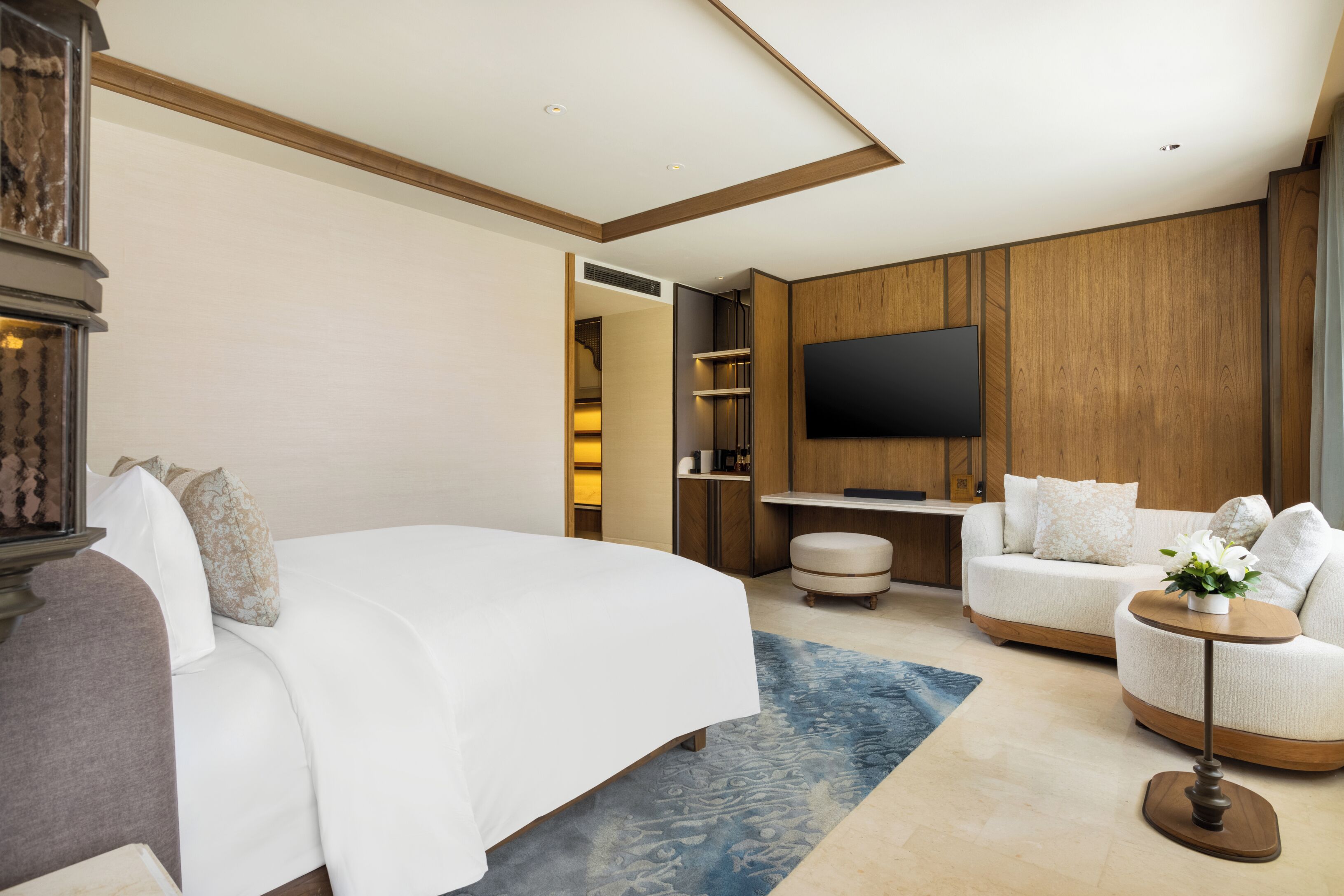 A hotel room with a large bed, a sofa, a TV mounted on the wall, and a small table with a plant.