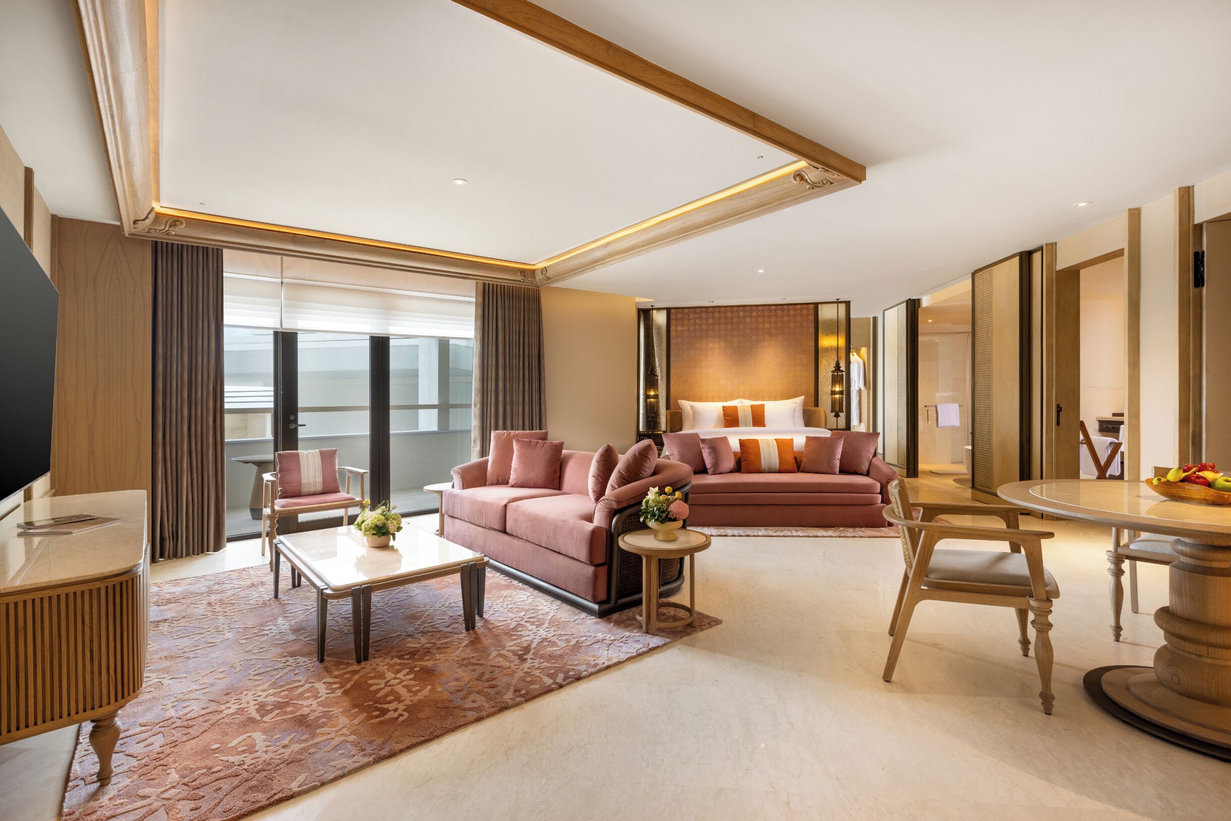 A modern hotel room with a sofa, a dining table, a coffee table, and a TV.