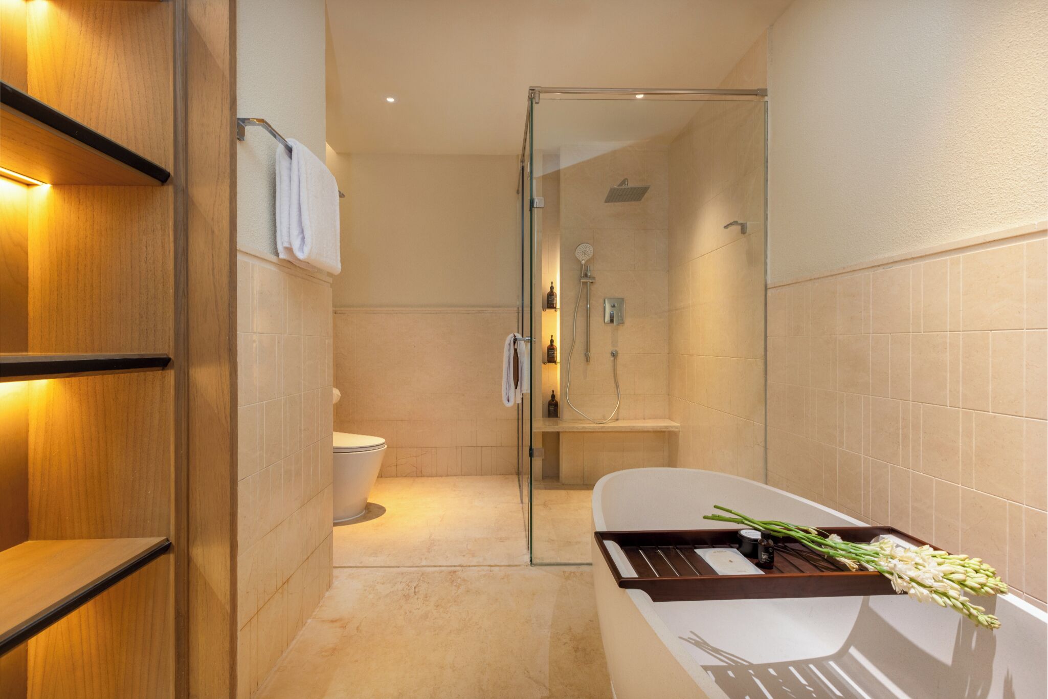 Ein modernes Badezimmer mit einer gläsernen Duschkabine, einer weißen Badewanne mit Ablagefläche und einem Holzregal.