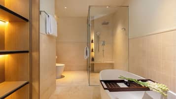 A modern bathroom with a glass-enclosed shower, a white bathtub with a tray, and a wooden shelf.