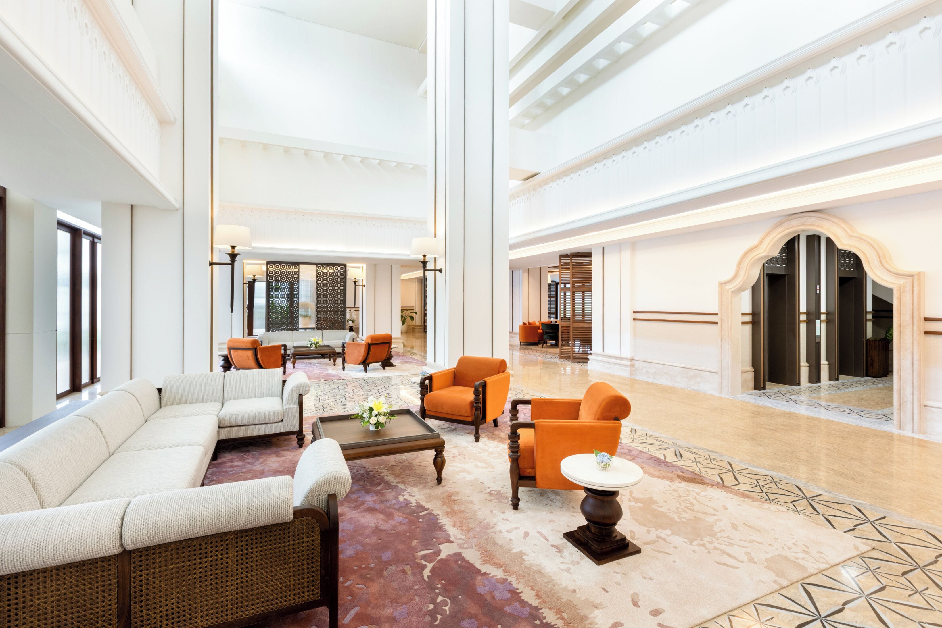 A spacious lobby with a high ceiling, a large sofa, several armchairs, a coffee table, and a patterned rug.