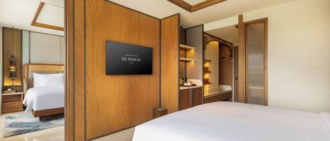 A modern hotel room with a large bed, a wooden panel wall, a flat-screen TV, and a bathroom with a mirror and towel rack.