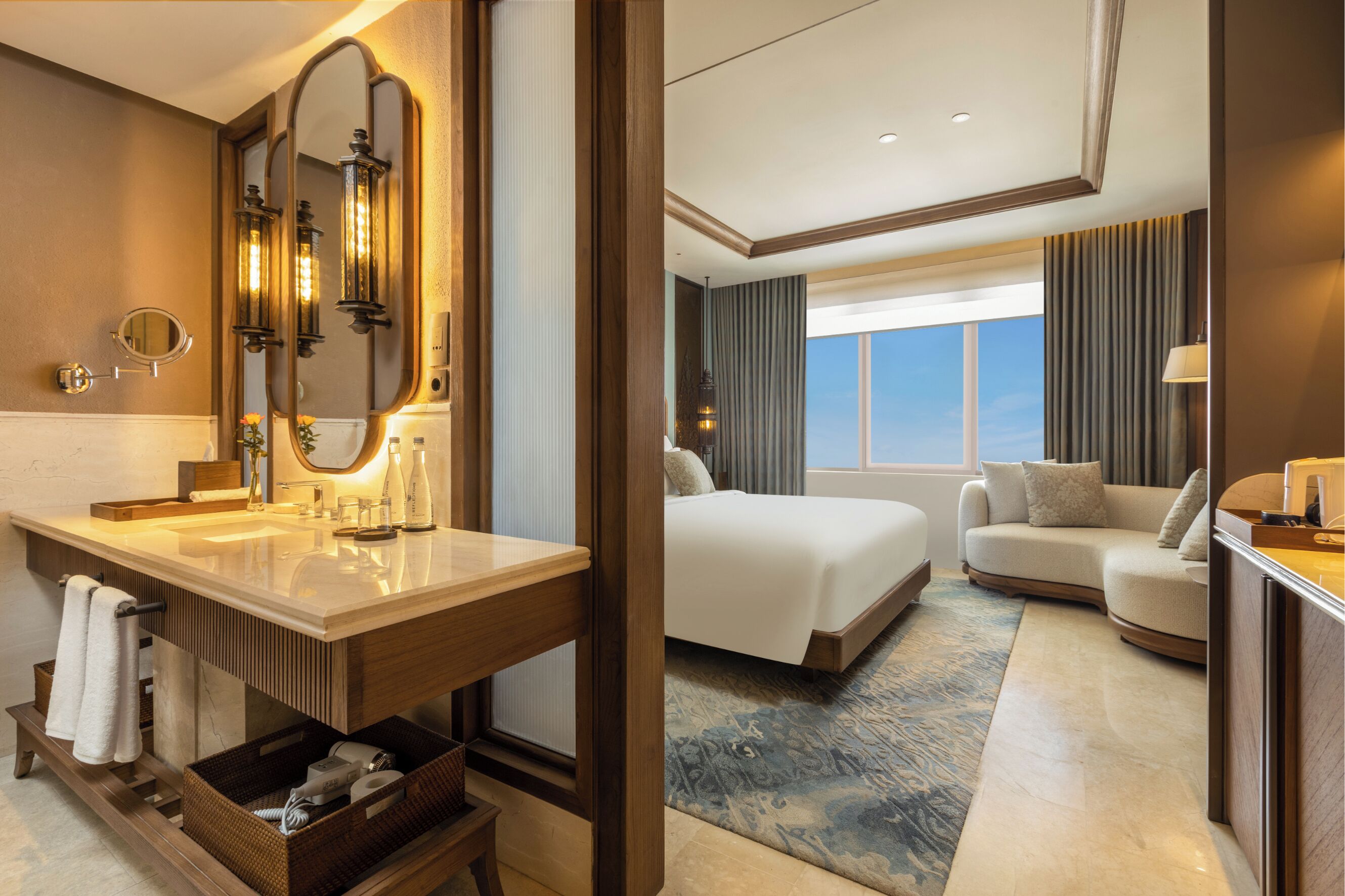 Une chambre d’hôtel avec un grand miroir, une coiffeuse en bois, un lit, un canapé et une vue sur le ciel.